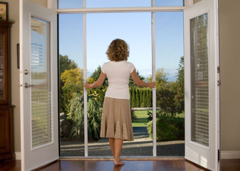 A women standing in the doorway opening her retractable sceen door overlooking her backyard.